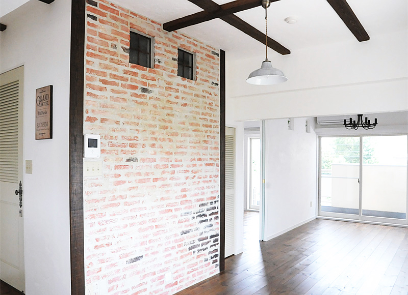 白い壁に映えるブリック仕上げの壁と天井の梁がフレンチカントリーな空間の部屋。